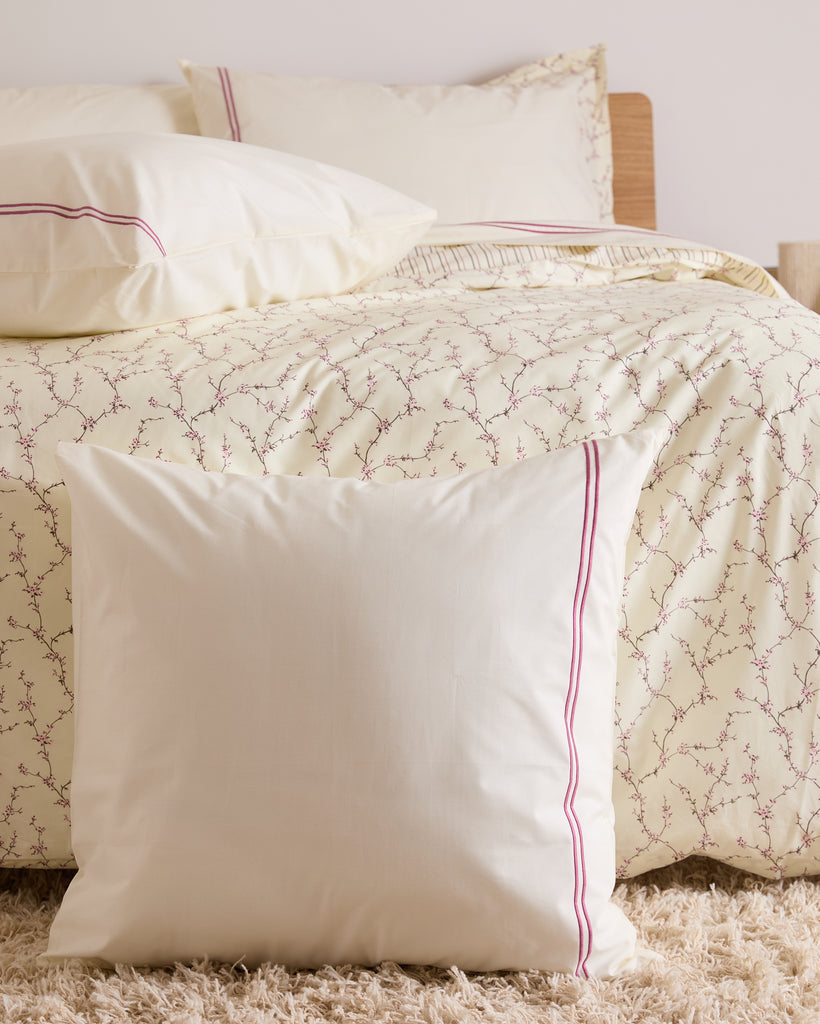 Cream pillow with red trim on a bed with floral-patterned bedding.