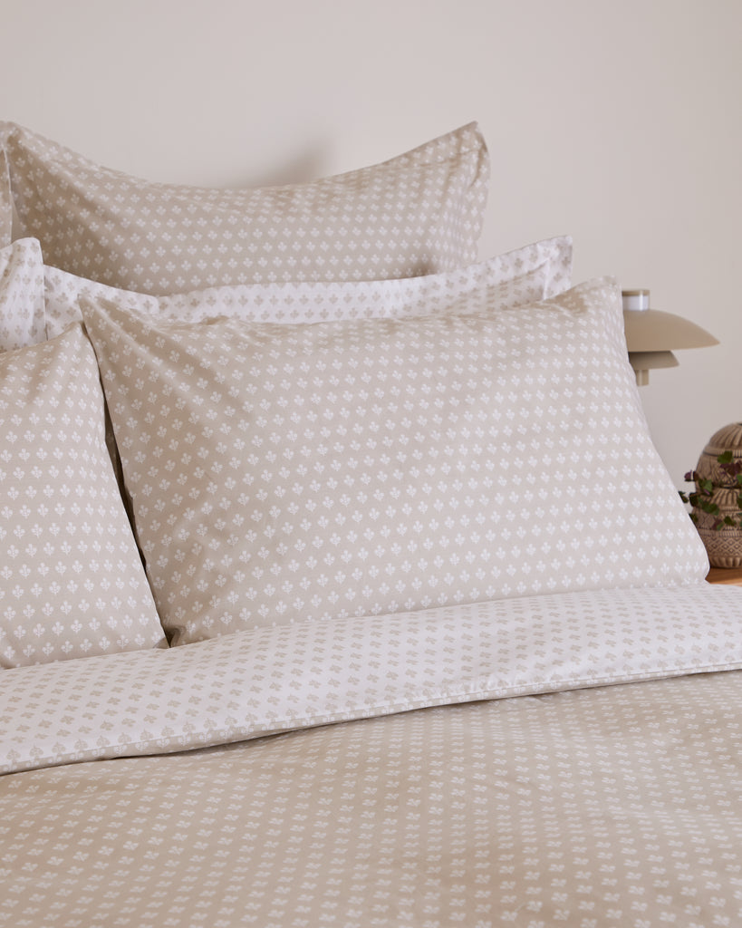 Beige patterned pillows and bedding on a bed with a neutral background